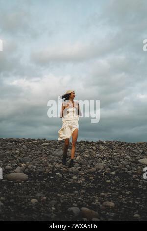 Junge glückliche tätowierte Frau in einem Kleid an einem windigen felsigen Strand. Stockfoto