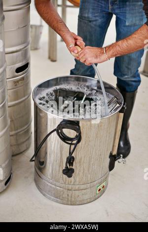 Brauerei, Mann und Hände im Tank im Werk für die Reinigung von Rohren, Fertigungswerkzeugen oder Maschinen. Industrie-, Arbeits- und Waschbehälter für die Brauerei Stockfoto
