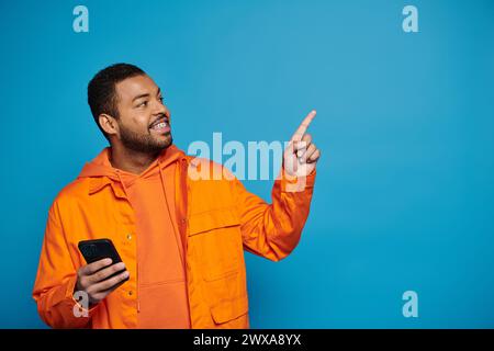 Charmanter afroamerikanischer junger Mann in orangefarbenem Outfit mit Smartphone, das den Finger nach oben zeigt Stockfoto