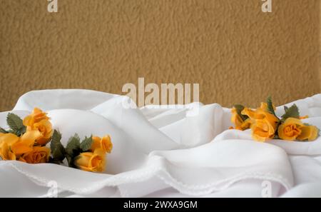 Horizontaler Hintergrund mit weißem Stoff und orangefarbenen Blumen gegen eine senffarbene Wand Stockfoto