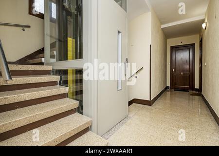 Landung eines Wohngebäudes mit einem Berater mit Glaswänden, grauer Metalltür und Terrazzo-Treppe. Stockfoto