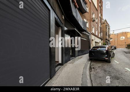 Geschäftsgebäude mit schwarzer Fassade im Erdgeschoss eines Gebäudes mit Fahrzeugen, die auf der Straße geparkt sind Stockfoto