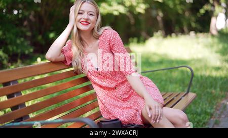 Glückliche junge Frau lächelt im Sommer auf der Parkbank Stockfoto