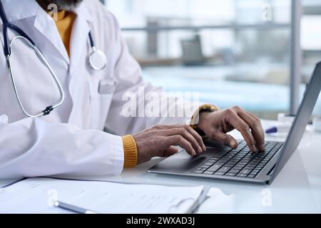 Seitliche Nahaufnahme einer nicht erkennbaren Arzteingabe auf Laptop-Tastatur am Arbeitsplatz im Kopierraum der Klinik Stockfoto