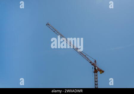 Ein roter Kran baut einen Neubau an einem sonnigen Tag vor blauem Himmel Stockfoto