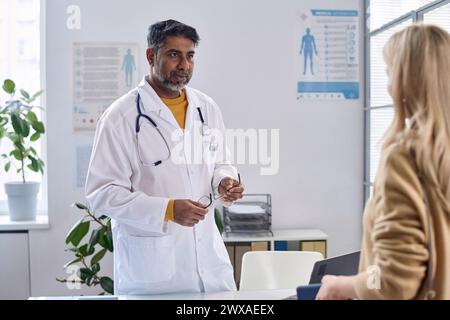 Porträt eines Oberärztes aus dem Nahen Osten mit Laborkittel und Begrüßung des Patienten im Kopierraum des Klinikbüros Stockfoto