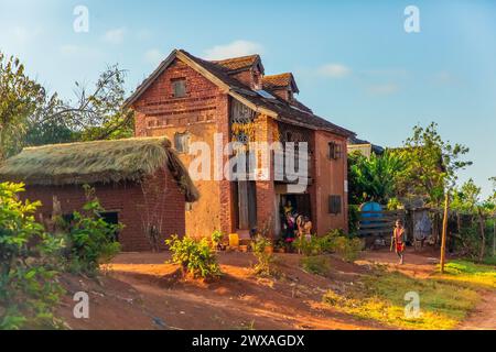 Madagaskar, 22. oktober 2023. Traditionelles zweistöckiges Backsteinhaus im Dorf Madagaskar bei Sonnenaufgang. Familie mit Kindern ist vor der Haustür. Maiskolben sind dr. Stockfoto