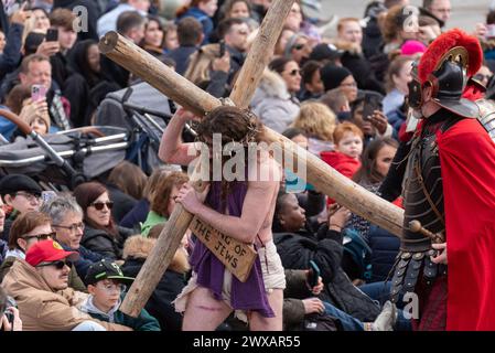 Trafalgar Square, London, Großbritannien. März 2024. Am Karfreitag am Osterabend präsentierte die Theaterbesetzung von Wintershall „die Passion Jesu“, ein Stück, das die Bibelgeschichte Christi durch die „Wunder“, das letzte Abendmahl, und die Kreuzigung durch die Römer, bevor sie wieder zur Auferstehung aufstehen, alle benutzten den Trafalgar Square als Bühne für dieses kostenlose öffentliche Ereignis. Eine große Menschenmenge von Tausenden, die auf den Platz gepackt sind, beobachtete, wie Christus vom Schauspieler Peter Bergin dargestellt wird. Jesus trägt das Kreuz Stockfoto