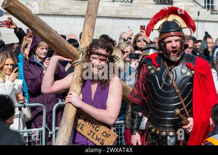 Trafalgar Square, London, Großbritannien. März 2024. Am Karfreitag am Osterabend präsentierte die Theaterbesetzung von Wintershall „die Passion Jesu“, ein Stück, das die Bibelgeschichte Christi durch die „Wunder“, das letzte Abendmahl, und die Kreuzigung durch die Römer, bevor sie wieder zur Auferstehung aufstehen, alle benutzten den Trafalgar Square als Bühne für dieses kostenlose öffentliche Ereignis. Eine große Menschenmenge von Tausenden, die auf den Platz gepackt sind, beobachtete, wie Christus vom Schauspieler Peter Bergin dargestellt wird, der hier das Kreuz trägt Stockfoto