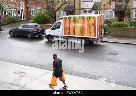 Ein Mann trägt Sainsburys Einkaufshaus gegenüber einem Parkplatz für Lieferwagen von Sainsbury vor einer Wohnterrasse in London England Großbritannien Stockfoto