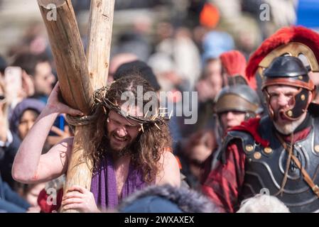 Trafalgar Square, London, Großbritannien. März 2024. Am Karfreitag am Osterabend präsentierte die Theaterbesetzung von Wintershall „die Passion Jesu“, ein Stück, das die Bibelgeschichte Christi durch die „Wunder“, das letzte Abendmahl, und die Kreuzigung durch die Römer, bevor sie wieder zur Auferstehung aufstehen, alle benutzten den Trafalgar Square als Bühne für dieses kostenlose öffentliche Ereignis. Eine große Menschenmenge von Tausenden, die auf den Platz gepackt sind, beobachtete, wie Christus vom Schauspieler Peter Bergin dargestellt wird, der hier das Kreuz trägt Stockfoto