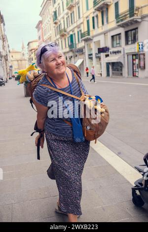 Eine ältere Frau reist durch Europa. Eine Großmutter mit Rucksack spaziert durch die Stadt in Italien. Alte Leute reisen gerne. Stockfoto