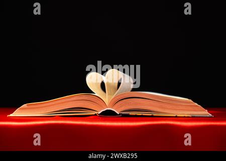 Die Seiten des Buches werden in Form eines Herzens auf einem roten und schwarzen Hintergrund gefaltet, um Text zu platzieren. Stockfoto