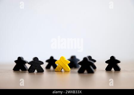 Eine einzelne gelbe Holzfigur hebt sich von schwarzen Holzformen auf einem schlichten Hintergrund ab. Stockfoto
