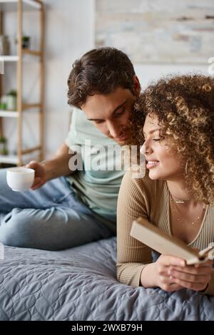 Gemütlicher Morgen mit einer lockigen jungen Frau, die ihr Buch liest, während sie von einem brünetten Mann umarmt wird Stockfoto