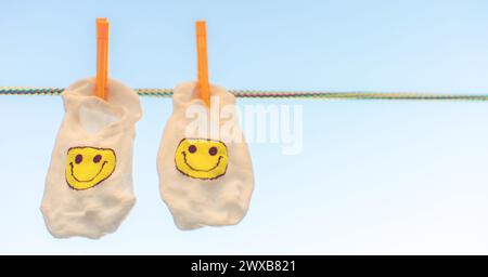 Weiße Socken mit gelbem Smiley-Emoticon hängen an einem Seil mit Wäschespins. Blauer Himmel Hintergrund. Stockfoto