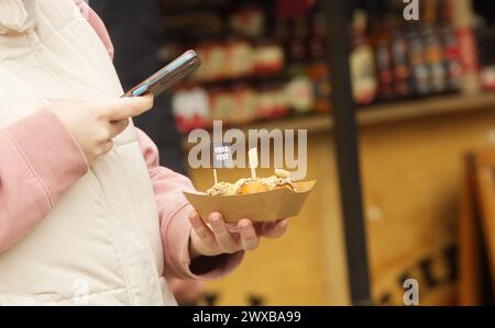 Frauenhände halten Dessert und Handy, Mitte des Frauenkörpers macht Selfie vom Dessert auf dem Bauernmarkt in Prag Naplavka. Stockfoto