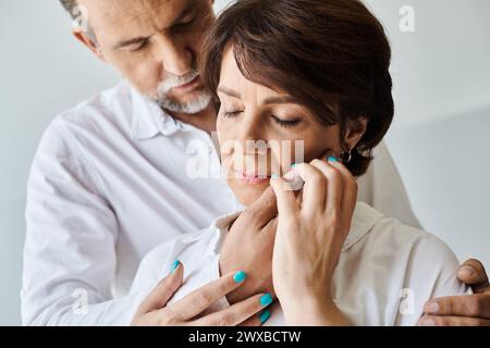 Porträt einer attraktiven Frau mittleren Alters, die die Hand des Mannes umarmt und ihr Gesicht auf grauem Hintergrund berührt Stockfoto