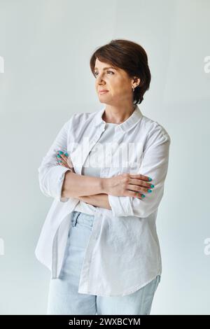 Porträt einer reiferen, schönen Frau, die mit gekreuzten Armen steht und wegblickt Stockfoto