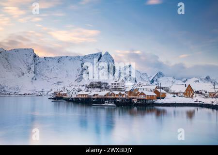 Traditionelle gelbe rorbuer-Hütten auf der Insel Sakrisoy, schneebedeckte Berge im Hintergrund, Sakrisoy, reine, Lofoten, Norwegen Stockfoto