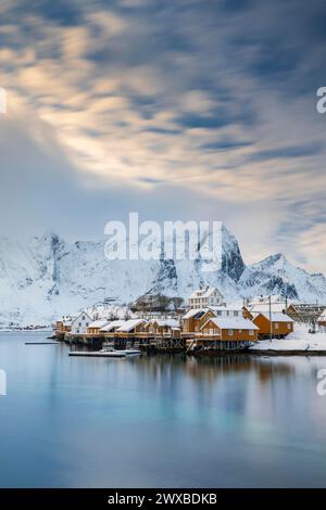 Traditionelle gelbe rorbuer-Hütten auf der Insel Sakrisoy, schneebedeckte Berge im Hintergrund, Sakrisoy, reine, Lofoten, Norwegen Stockfoto