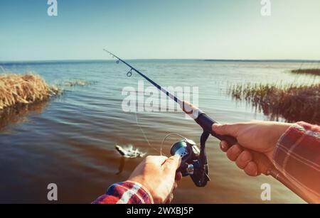 Der Fischer fängt Fische am Ufer des Sees, hält seine Hände drehend gegen den wunderschönen See und den bewölkten Himmel. Stockfoto