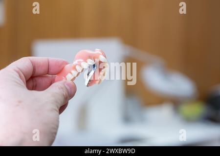 Ein Prothesentechniker hält eine Prothese, an der er gerade arbeitet. Im Hintergrund ist das Prothesenlabor unscharf. Stockfoto