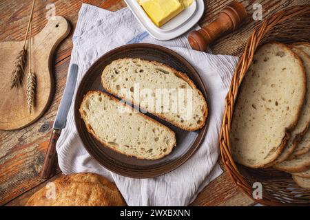 Zwei Scheiben handwerkliches Brot auf einem Teller neben Butter und einem Brotkorb, die eine heimelige Atmosphäre schaffen Stockfoto