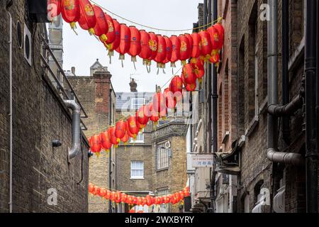 Rote chinesische Laternen erhellen eine enge und isolierte Seitenstraße in Chinatown. Rohrleitungen sprießen von den Wänden einer schattigen Gasse. Stockfoto