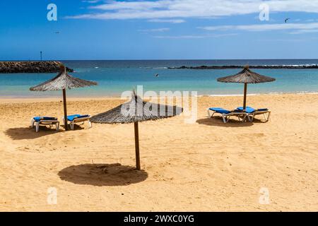 Ein leerer Strand in der Nebensaison mit Strohschirmen und blauer Sonnenliege. Playa del Castillo , Fuerteventura, Kanarische Inseln, Spanien Stockfoto