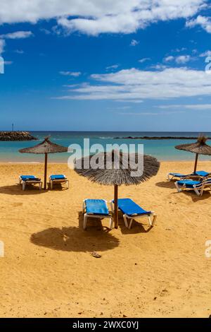 Ein leerer Strand in der Nebensaison mit Strohschirmen und blauer Sonnenliege. Playa del Castillo , Fuerteventura, Kanarische Inseln, Spanien Stockfoto