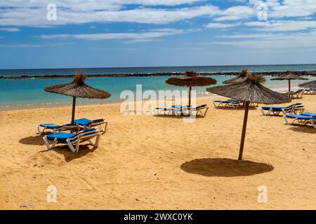 Ein leerer Strand in der Nebensaison mit Strohschirmen und blauer Sonnenliege. Playa del Castillo , Fuerteventura, Kanarische Inseln, Spanien Stockfoto