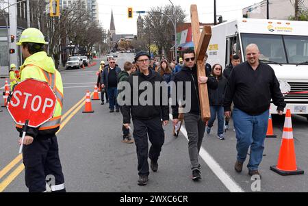 Victoria, British Columbia, Kanada, 29. März 2024 - Ein Mann trägt ein großes Holzkreuz an einer Straßenreparaturcrew in der Innenstadt von Victoria während der jährlichen KarfreitagsPassionsprozession in der Christ Church Cathedral (Anglican) vorbei. Don Denton/Alamy Live News Stockfoto