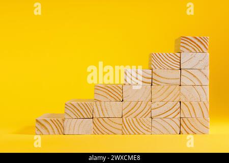 Holzblöcke, die eine Treppe bilden, auf gelbem Hintergrund. Erfolgsleiter Stockfoto