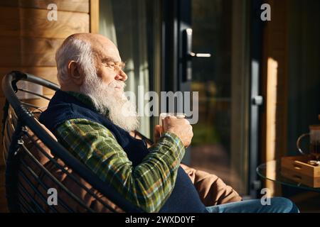 Ein älterer Mann sitzt auf der Veranda mit einer Tasse Tee Stockfoto
