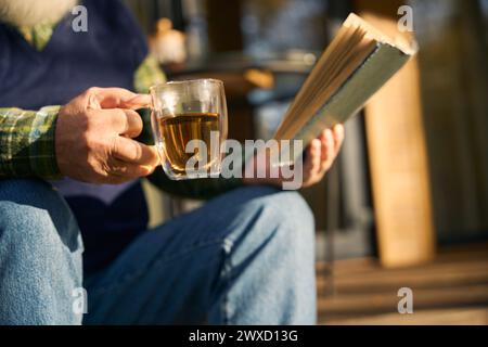 Ein älterer Mann sitzt mit einem Buch auf der Veranda Stockfoto