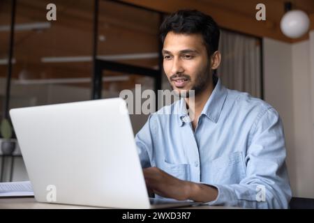 Positiver indischer Geschäftsmann in Gelegenheitsarbeit am Laptop Stockfoto
