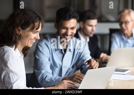 Fröhliche multiethnische Kollegen, die über Laptop reden und lachen Stockfoto