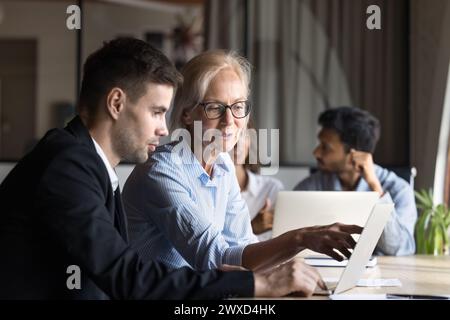 Seriöse Senior Business Coach Frau zeigt jüngeren Mitarbeitern Inhalte Stockfoto