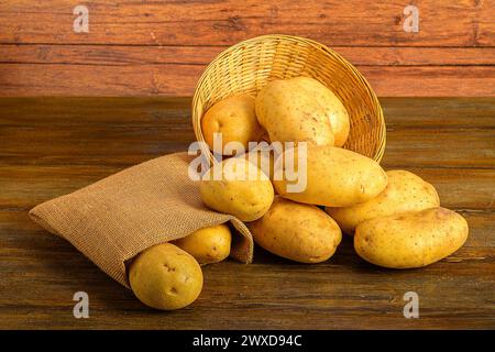 Ein Korbkorb mit Kartoffeln und einem Sack auf einem Holztisch. Stockfoto