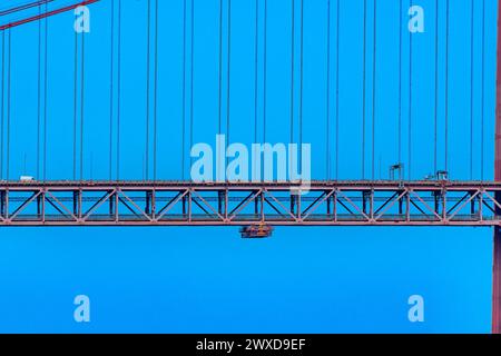 Teil der 25 de Abril Hängebrücke mit roten Stahlseilen, die die Struktur stützen, wo der Straßenverkehr nach Lissabon führt, und ein Doppelseil Stockfoto