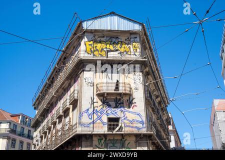 Fassade voller Straßenkunst und Graffiti auf einer Straße in Portugal mit Straßenbahnschienen und Kabeln. Stockfoto