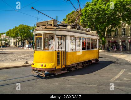 Berühmte und typische alte gelbe portugiesische Straßenbahn, wunderschön dekoriert und erhalten, fährt auf den Spuren eines Kreisverkehrs einer typischen Lissabon Straße i Stockfoto