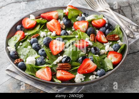 Spinatsalat mit Erdbeeren, Heidelbeeren, Käse und Pekannüssen mit Honigdressing in Nahaufnahme auf einem Teller auf dem Tisch. Horizontal Stockfoto