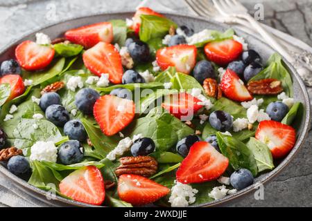 Vitaminsalat aus frischem Spinat, Erdbeeren und Heidelbeeren mit Käse und Pekannüssen mit Honig-Dressing in einem Teller auf dem Tisch. Horizontal Stockfoto