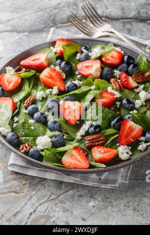 Frischer Salat aus Spinat, Erdbeeren und Heidelbeeren mit Käse und Pekannüssen mit Honig-Dressing in einem Teller auf dem Tisch. Vertikal Stockfoto