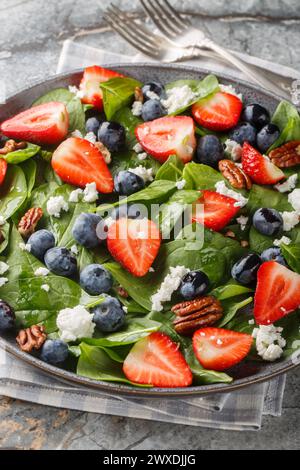 Frühlingssalat aus Spinat, Erdbeeren, Heidelbeeren, Ziegenkäse und Pekannüsse in Nahaufnahme auf einem Teller auf dem Tisch. Vertikal Stockfoto