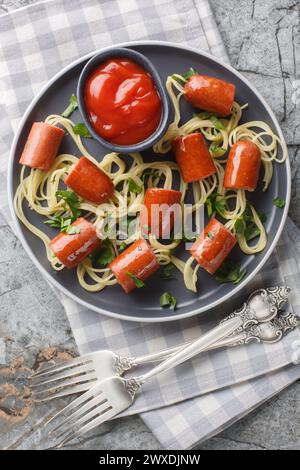 Festliche Vorstellung von Spaghetti mit Würstchen und Ketchup-Nahaufnahme auf einem Teller auf dem Tisch. Vertikale Draufsicht von oben Stockfoto