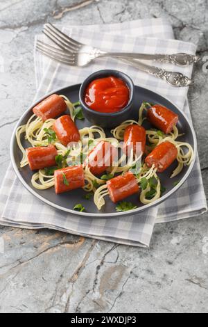 Festliche Vorstellung von Spaghetti mit Würstchen und Ketchup-Nahaufnahme auf einem Teller auf dem Tisch. Vertikal Stockfoto