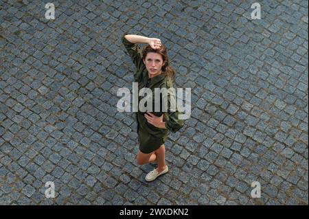 Blick von oben auf die junge Frau schaut nach oben. Schöne Frau posiert, während sie draußen steht. Junge glückliche Frau, die Sommerferien genießt. Blick von oben. Stockfoto